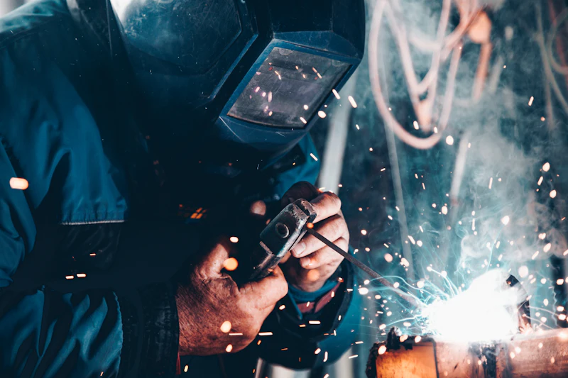 A welder joining steel components as sparks fly in a workshop